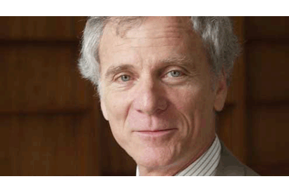A person with short gray hair and light skin is shown in this headshot. They are wearing a light-colored suit jacket and a striped dress shirt, looking directly at the camera with a slight smile. Recently appointed as Dean, Edward Wasserman stands against a blurred background.