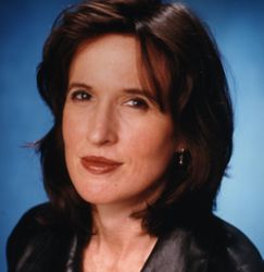 A woman with shoulder-length brown hair and wearing a dark blouse is pictured against a blue background. With a serious expression, she looks directly at the camera, embodying the investigative spirit of Berkeley Journalism.