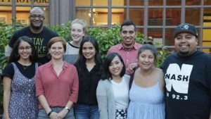 A group of nine Hispanic journalists, members of the National Association of Hispanic Journalists, stand closely together outside in front of a building. They are smiling and casually dressed, with greenery behind them. The group includes a mix of men and women of varying ages.
