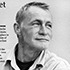 A grayscale image of a journalist looking slightly to the right. The individual has short hair and is wearing a buttoned shirt with a collar. There is partially visible text on the left side of the image, hinting at an award. The background is plain and light-colored.