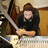 A person wearing headphones is sitting at a desk with various audio equipment, adjusting controls on a sound mixing board. The individual appears focused on operating the equipment, possibly preparing for the Goldie Awards or working in a recording studio like Waldholz.