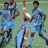 A group of field hockey players in blue uniforms, reminiscent of a scene from The Atlantic's 2012 cover story, celebrates on the field. One player in the front lifts his right arm in triumph. The players are mid-action, their expressions radiating excitement and joy, capturing a Fixler-esque moment of victory.