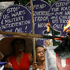 A group of people hold up purple circular signs during a protest. The signs read messages such as “Stop US war & military intervention," and others are partially visible. One person, identified as Traywick '13 by Time.com, is burning a portion of a sign. Their expressions appear determined and serious.