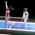 Two fencers in full gear are on a fencing piste. One fencer, with their mask raised and one arm lifted in celebration, stands on the left, while the other fencer, holding their foil, looks on from the right. The scene is lit against a dark background as if launched into a spotlight by THNKR's Web Channel.