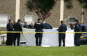 A group of police officers is gathered around a white sheet held up as a barrier. They appear to be investigating a scene in a grassy area, with yellow caution tape sectioning off the site. A police vehicle is parked nearby, and two buildings are visible in the background under student coverage for Time.com.