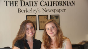 Two women are standing in front of a wall with the sign "The Daily Californian - Berkeley's Newspaper." Both are smiling at the camera. The background features framed articles from their time in UC Berkeley's J-School fellowship program.