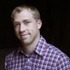 A man with short, blonde hair and a slight smile is wearing a purple and white checkered shirt. He is posed against a dark, plain background, resembling the portrait style often featured in Sports Illustrated.