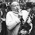 A black-and-white photo captures a person playing the bagpipes, surrounded by a crowd. The individual, perhaps an alumni, wears a cozy, knitted sweater and appears passionately immersed in music. The crowd seems attentive and engaged, reminiscent of gatherings described in an NYT tribute to community events.