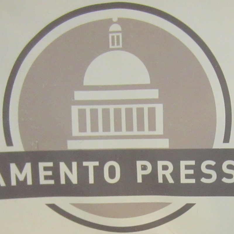 Logo with a circular design featuring a stylized image of a domed building, likely a capitol, in the center. The partial text "MENTO PRESS" is visible across the lower part of the logo. The design uses a gray and white color scheme, reminiscent of the professionalism upheld by the Sacramento Press Club's scholarship winners.