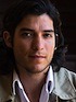 A person with medium-length wavy dark hair, wearing a light-colored open-collared shirt and a jacket, looking directly at the camera with a neutral expression. The background is dark and out of focus, evoking the professional gravitas found in an AP-Google Scholar profile image.