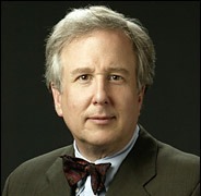 A middle-aged man with gray hair, wearing a dark suit and a bow tie, is posing against a black background. He has a neutral expression and is looking directly at the camera, reminiscent of a seasoned Berkeley Journalism professor.