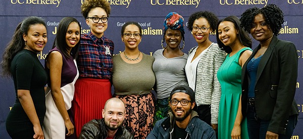 A diverse group of ten individuals smiles for a photo in front of a UC Berkeley Journalism backdrop. The group consists of eight women and two men, all dressed in various casual and semi-formal outfits, reflecting a joyful and inclusive atmosphere.