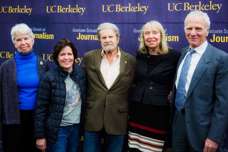 A group of five people stands in front of a UC Berkeley backdrop, appearing to be at an event associated with Berkeley Journalism's Graduate School. The individuals are smiling and dressed in business casual attire.