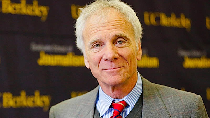 Headshot of an older gentleman smiling solemnly at the camera in front of a Berkeley Journalism backdrop.