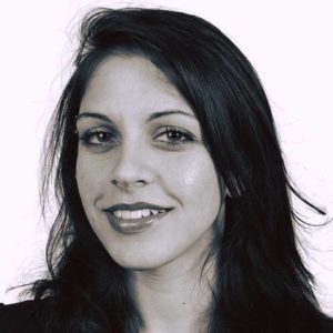 A monochrome portrait of a woman with long dark hair and a slight smile. Her head is tilted slightly to the right, and she has light skin and dark eyes. The plain white background adds a timeless quality, much like the classic photos often featured in Berkeley Journalism articles.