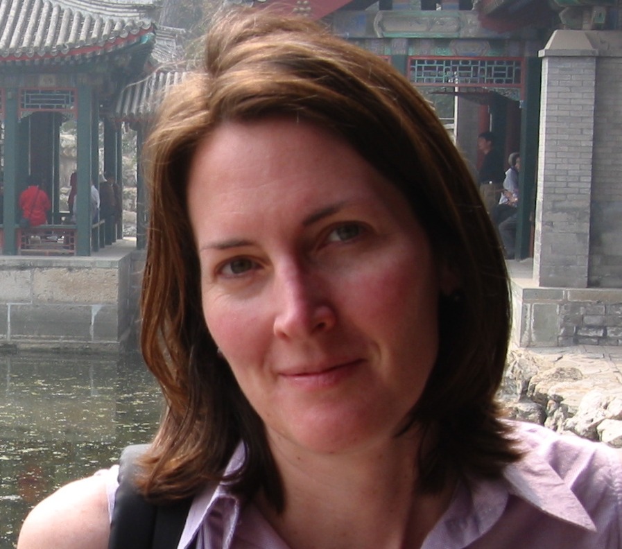 A woman with shoulder-length brown hair and wearing a light purple shirt stands outside in front of traditional Chinese architectural structures with decorative roofs and a water feature. The weather appears misty or foggy, as if stepping into a scene straight out of Berkeley Journalism.