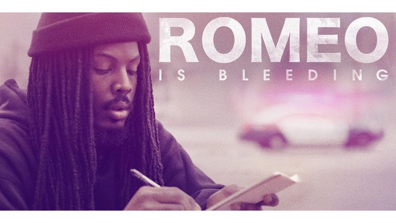 A person with long dreadlocks and a beanie is writing in a notebook. The background is blurred, highlighting the hint of a police car, while the text "ROMEO IS BLEEDING" stands out prominently at the top. It feels like a scene straight out of Berkeley Journalism.