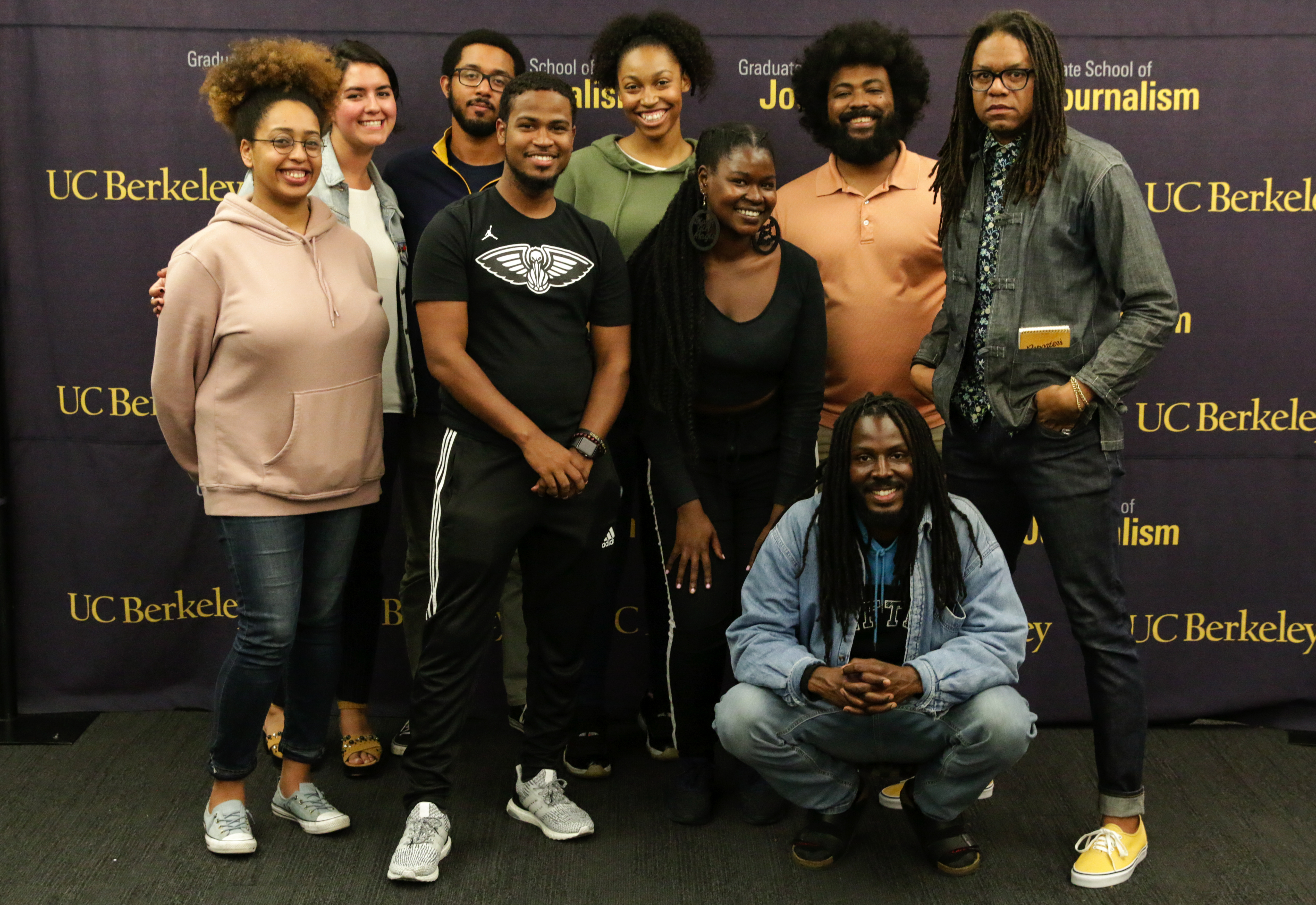 Group photo of seven African American students and their guests standing in front of a Berkeley Journalism logo'd background.