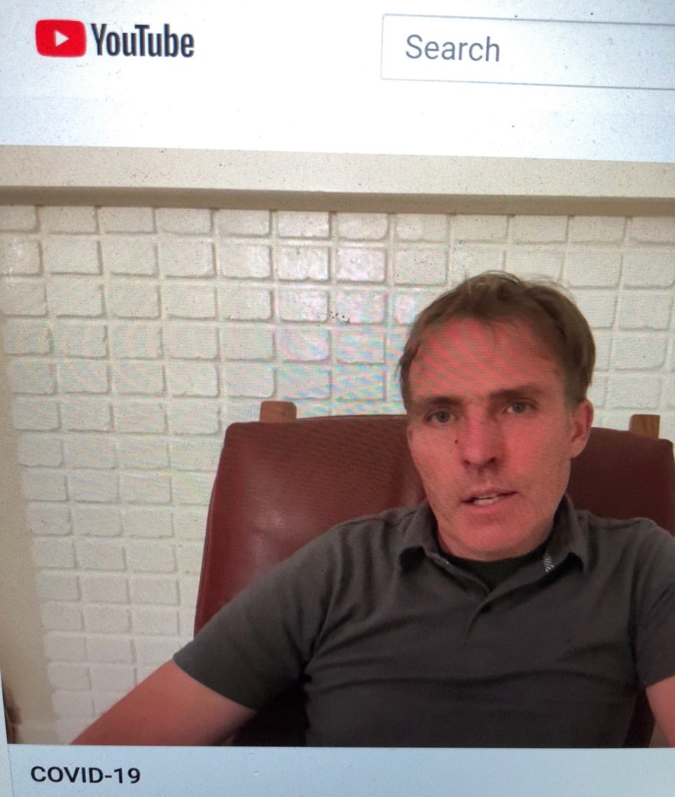 A man with short hair, wearing a dark polo shirt, is sitting in a brown chair speaking to the camera. The word "COVID-19" is visible at the bottom of the screen, while the YouTube logo and search bar are at the top left. This segment appears to be produced by Berkeley Journalism.