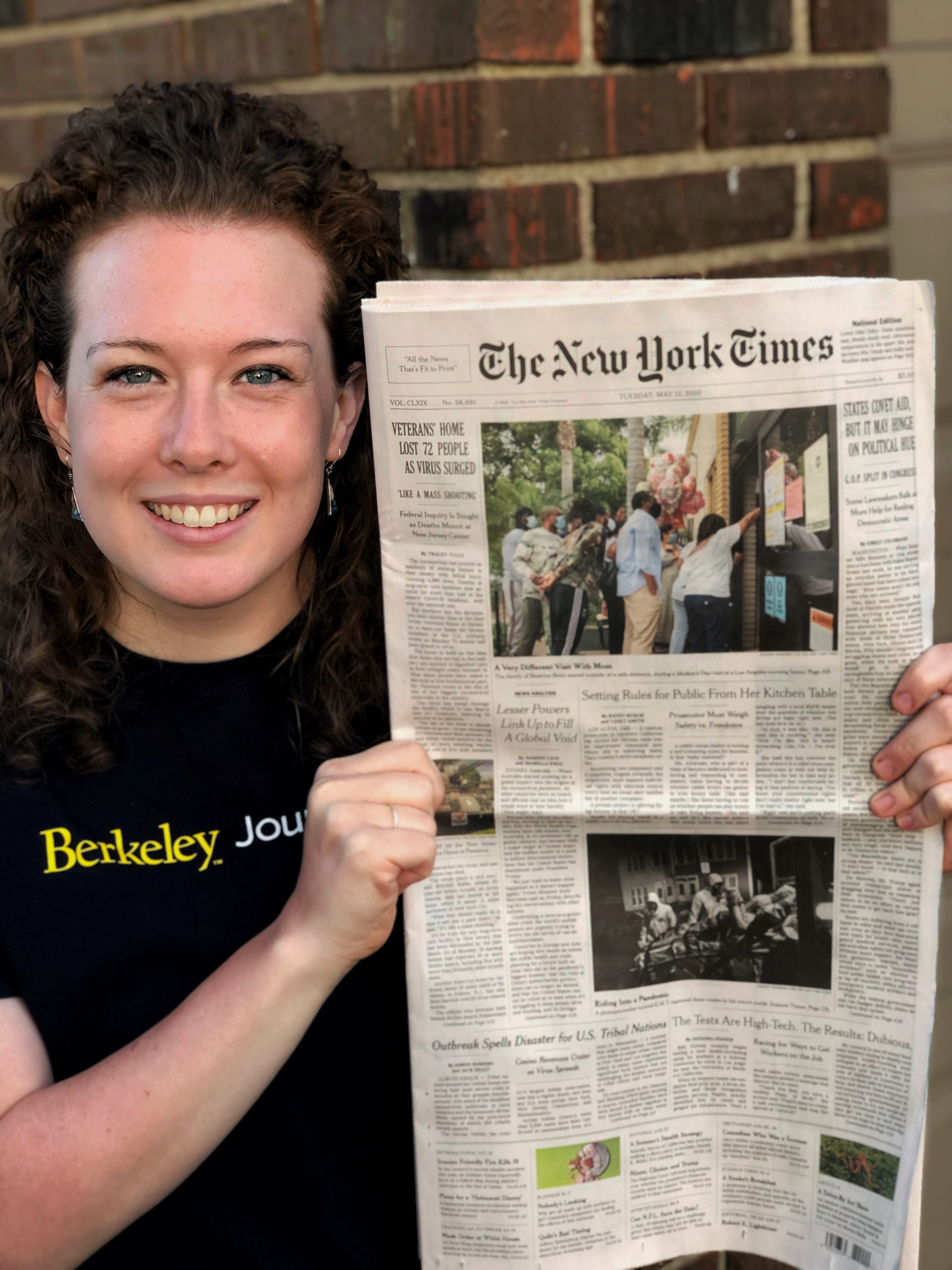 Casey Smith (’20) holding up the May 12, 2020 front page of The New York Times wearing a J-School tshirt smiling.