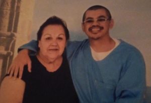 A smiling man in blue clothing with glasses, affiliated with Berkeley Journalism, has his arm around an older woman with short dark hair, also smiling. They stand close together in front of a neutral background.