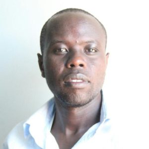 A man with short hair and a trimmed beard is looking directly at the camera. He is wearing a light blue shirt with the collar slightly open, standing against a plain white background, exuding the confidence of someone who could be in Berkeley Journalism.