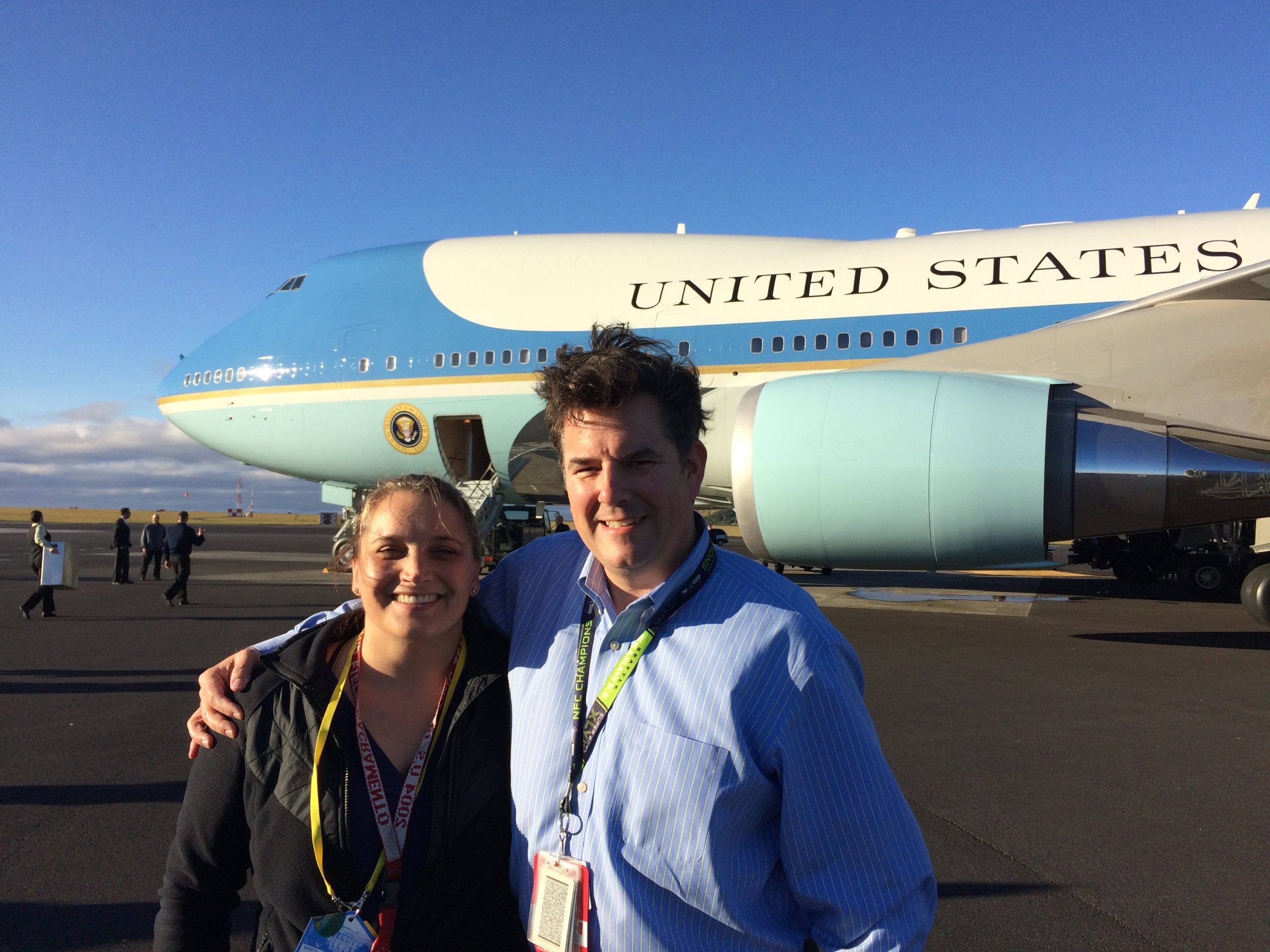 A smiling man and woman stand arm in arm in front of a large airplane with 