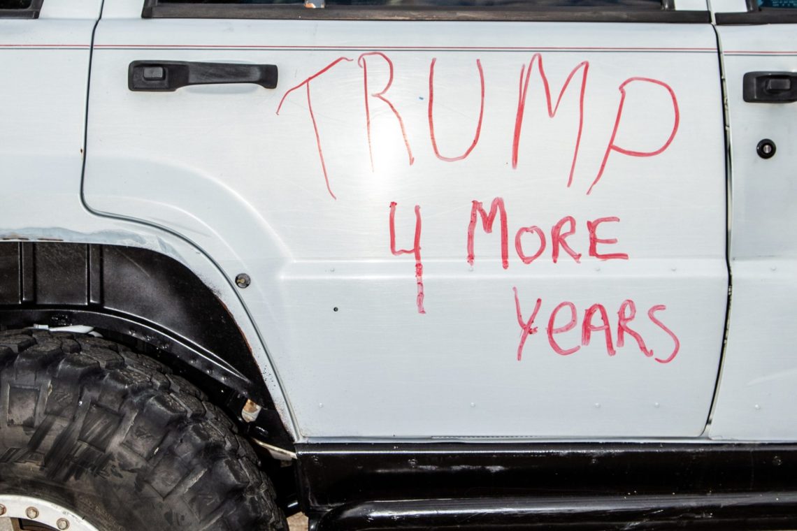 A vehicle door with "TRUMP 4 More Years" written in red marker. The image shows a portion of a white vehicle with black door handles and large tires, capturing a moment that could pique the interest of Berkeley Journalism students reporting on political expression.