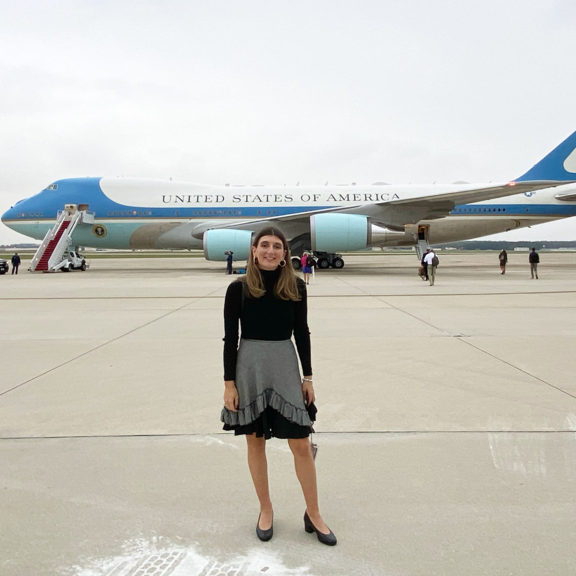 A person stands smiling on a tarmac in front of a large aircraft with 