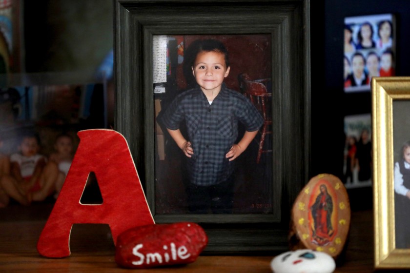 A framed photograph of a young boy standing with his hands on his hips, dressed in a checkered shirt, is displayed on a shelf. Surrounding the photo are decorative items including a red letter 