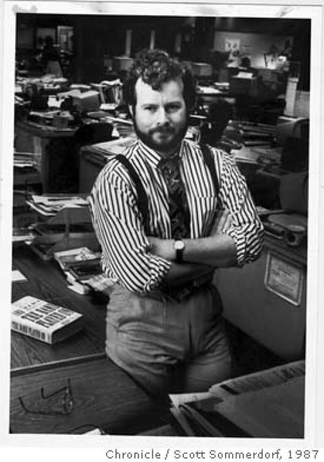 A man with a beard and mustache, wearing a striped shirt and suspenders, stands confidently with his arms crossed over his chest in an office with desks and papers scattered around. The photo, dated 1987 and credited to Scott Sommerdorf, Chronicle, reflects the essence of Berkeley Journalism.
