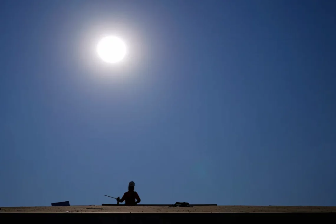 A roofer works on top of a housing development while the sun shines brightly behind them, during a June 2021 heatwave.