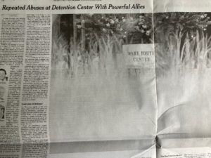 A newspaper is open to an article titled "Repeated Abuses at Detention Center With Powerful Allies" by Meg Shutzer in The New York Times. The article includes a black-and-white photograph showing a sign that reads "WARE YOUTH CENTER," partially obscured by plants in the foreground.