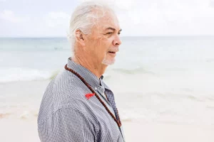 Ian Smith stands outside on the beach wearing a light colored shirt.