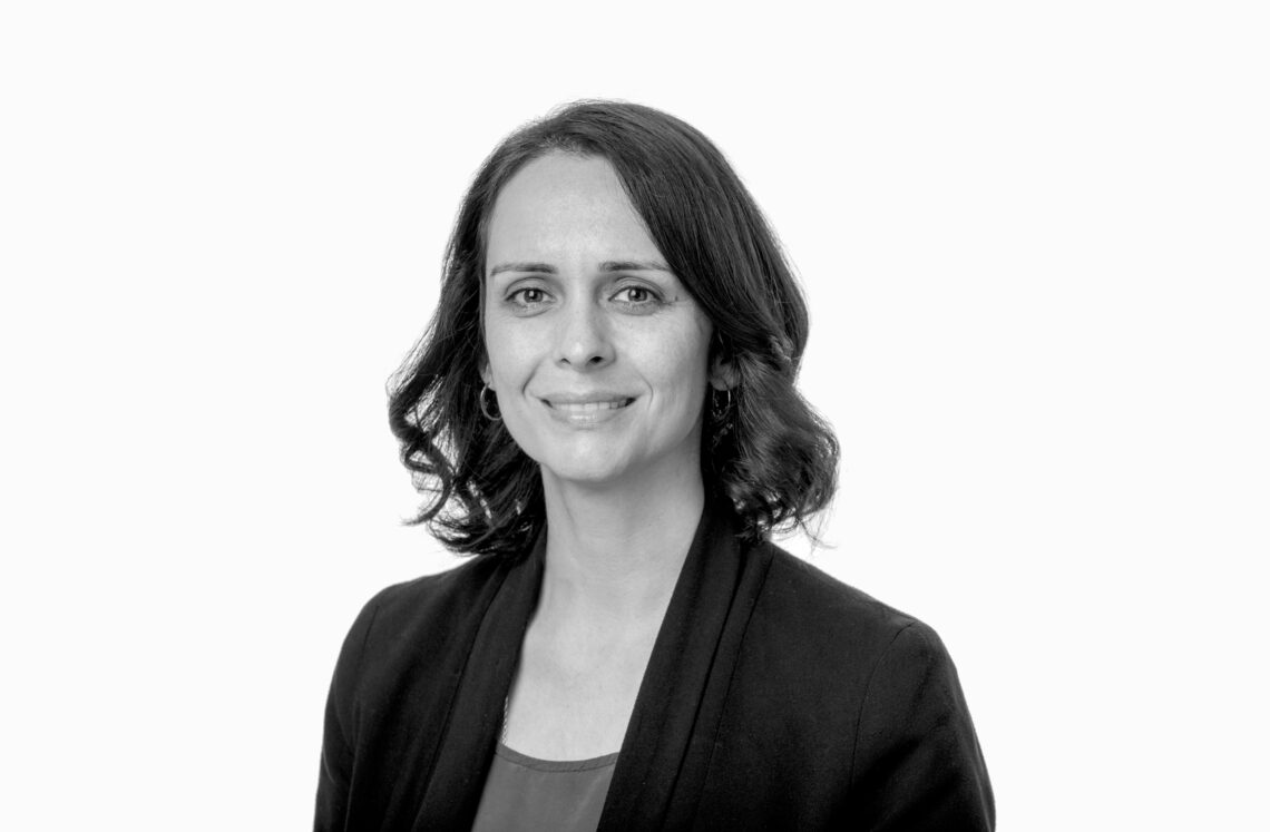 A black and white headshot of a middle aged woman. She is wearing a blazer and has shoulder length hair with waves at the ends.