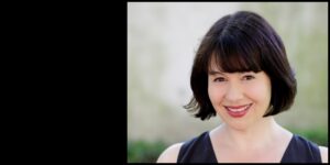 A woman with short, dark hair and bangs is smiling at the camera. She is wearing a sleeveless black top. The background is blurred with a mix of light colors, suggesting an outdoor setting. She has the assured gaze of a journalist ready for an engaging conversation.