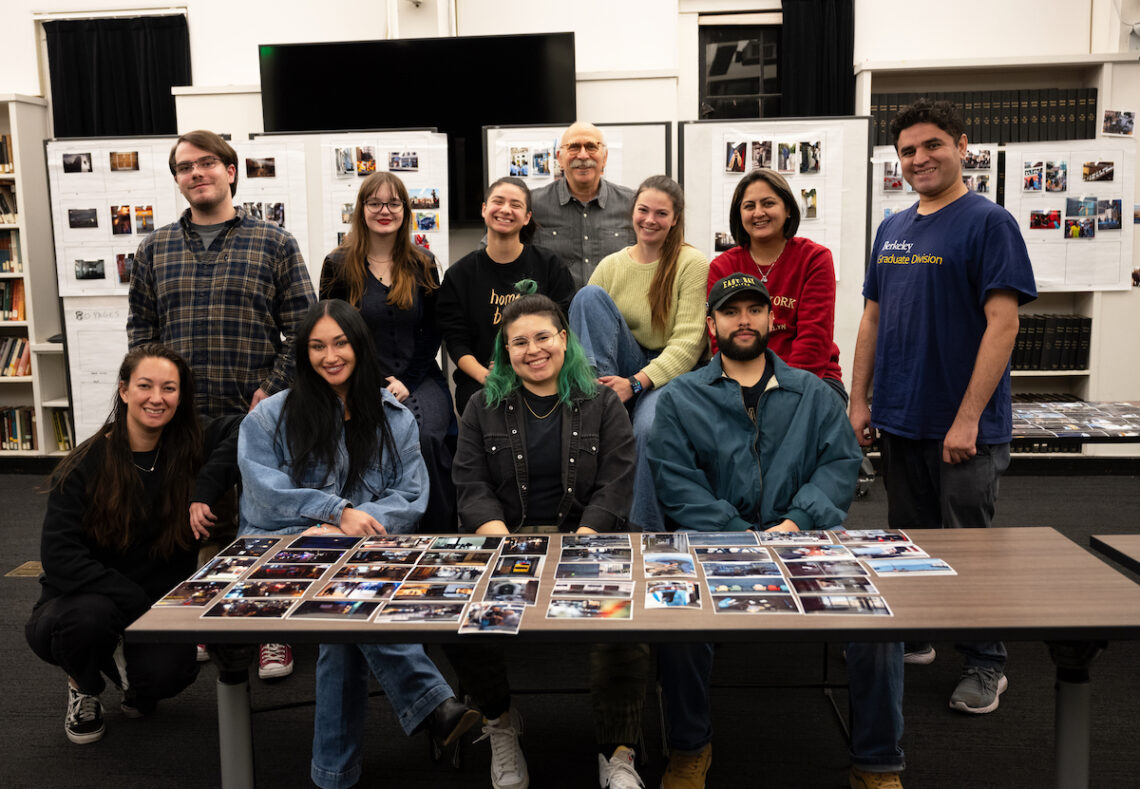 Group photo of students posed in front of a long table featuring their photographs smiling.