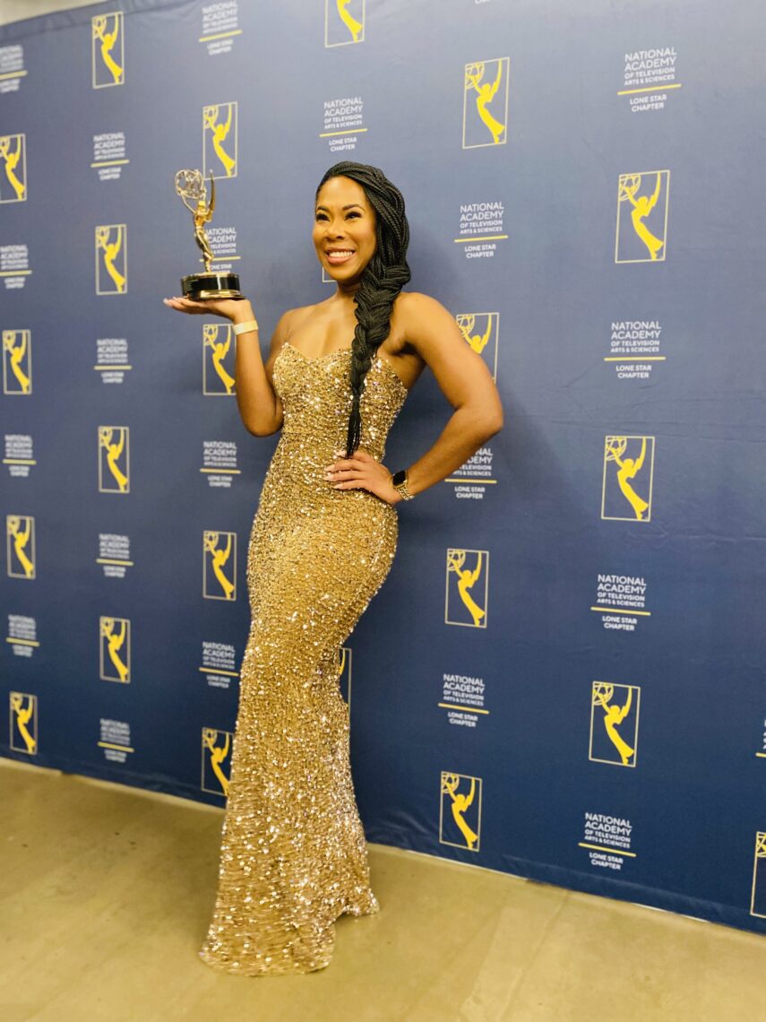 Photo of an African American woman wearing a beautiful gold beaded strapless gown holding an Emmy statue with her hand on her hip smiling on the red carpet.