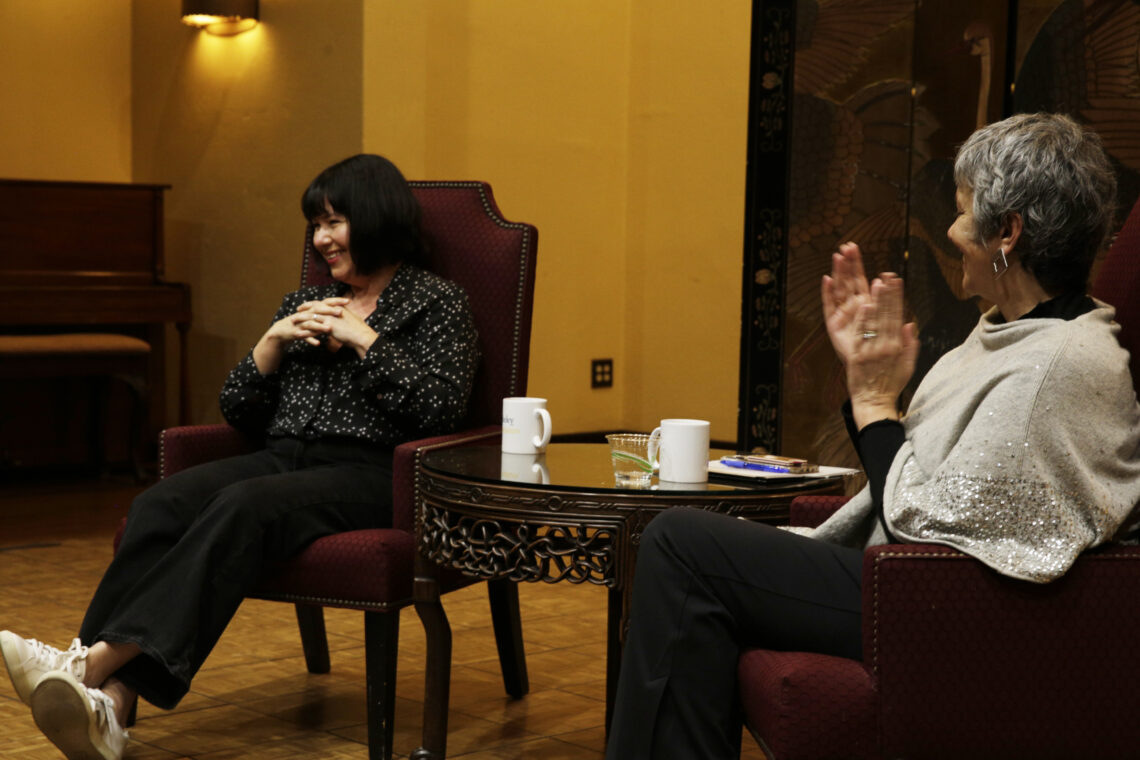 Photo of Michelle Goldberg and Dean Geeta onstage at the Bancroft Hotel clapping and smiling in chairs next to one another.