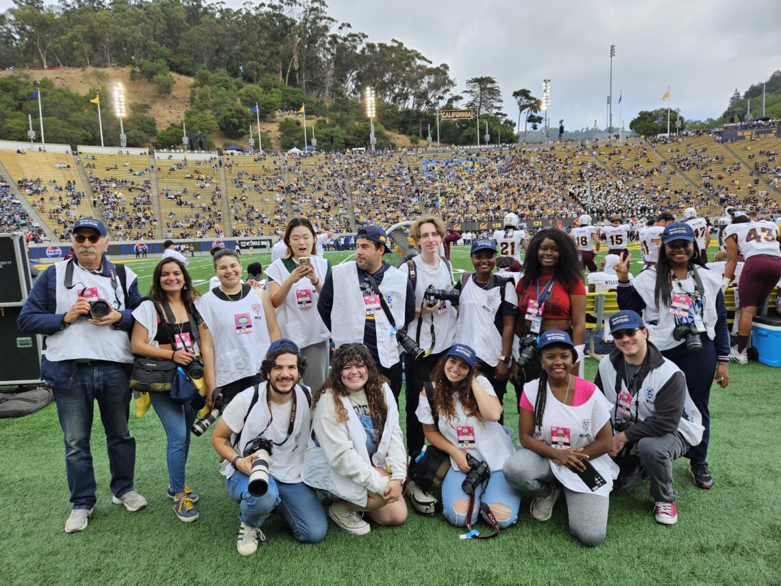 Photo of large group of student photographers posted together on a football field wearing cameras.