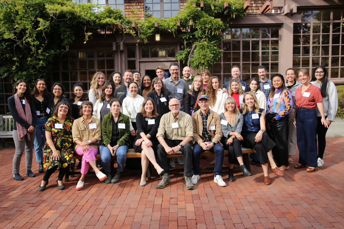 Group photo of alumni of the documentary film program at UC Berkeley standing or sitting in 4 rows in the courtyard of North Gate Hall smiling.