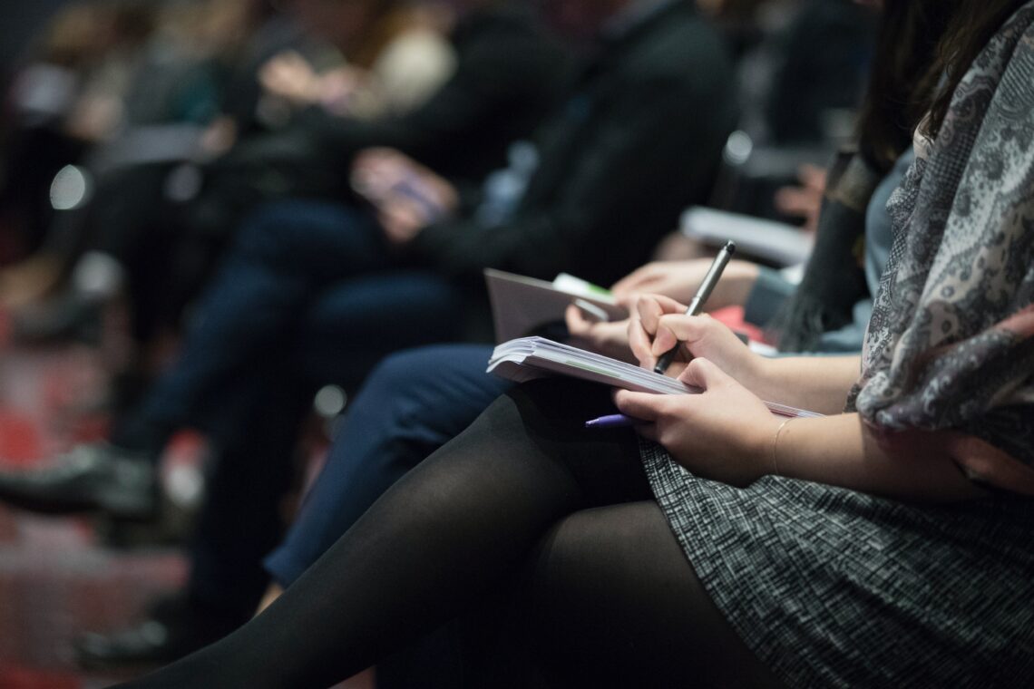 woman takes notes at an event. Only hands and legs visible.