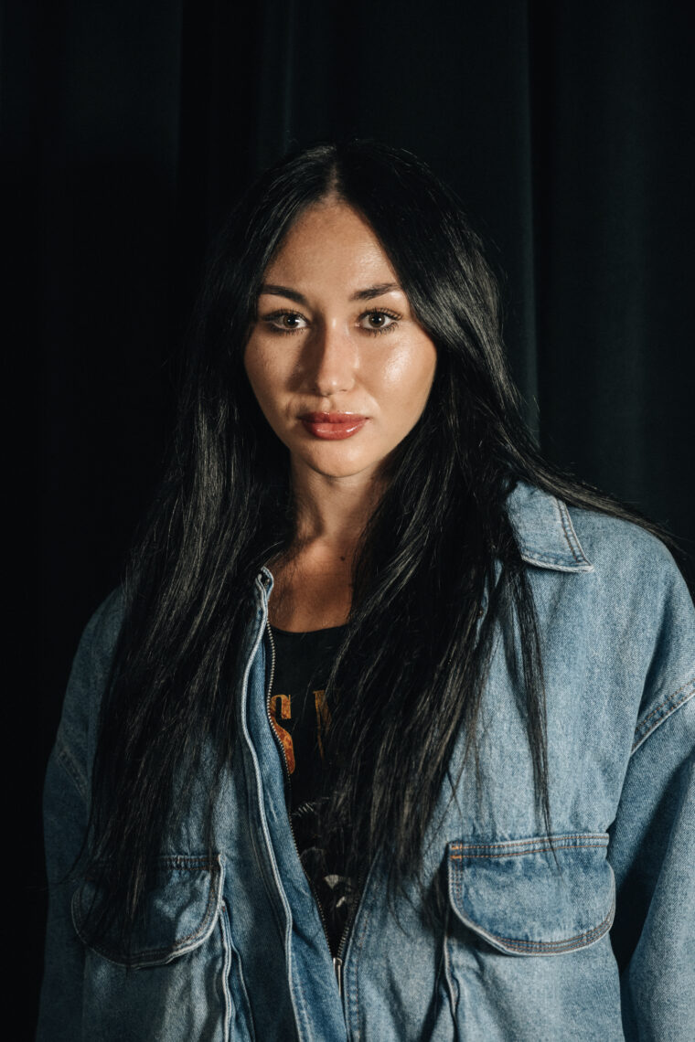 A woman with straight black hair wearing a jean jacket is posed for the camera.