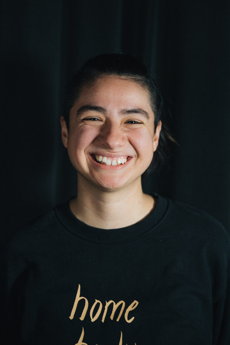 Gisselle Medina. A young student in a black crew neck with short hair tied up in a pony tail, smiling widely for the camera. 