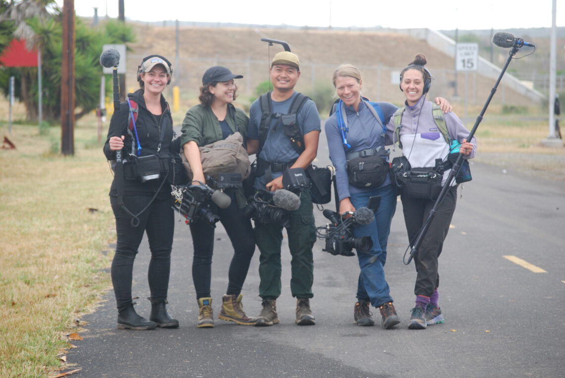 Pictured from left to right: Mallory Newman, ​Kelin Verrette, Rafael Roy, Lisa Hornak and Anna Kayes. They are pictured outside with big smiles holding media crew gear on the side of the road. 