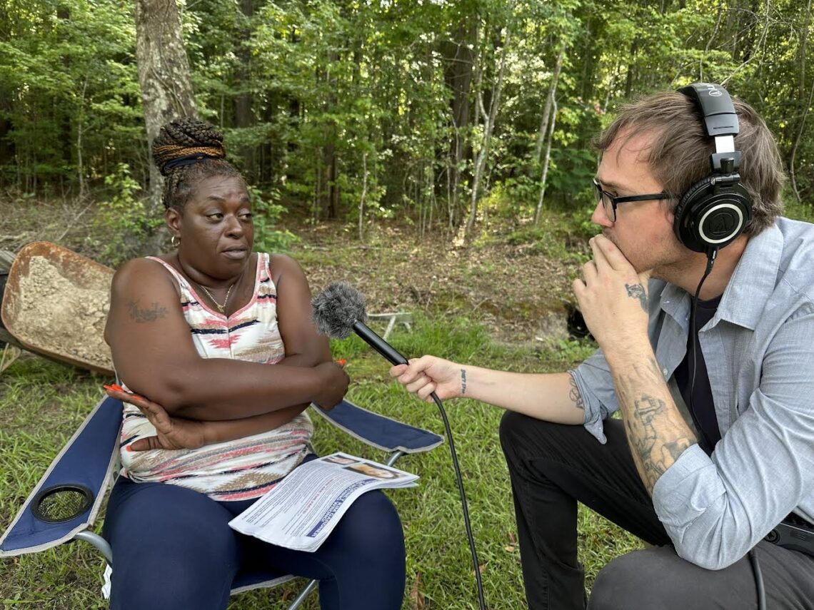 Photograph of a reporter wearing headphones holding out a microphone to a woman he is interviewing.