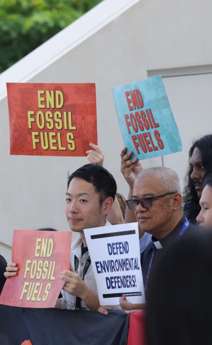 A group of people holding signs that say "END FOSSIL FUELS" and "DEFEND ENVIRONMENTAL DEFENDERS," advocating for climate action.