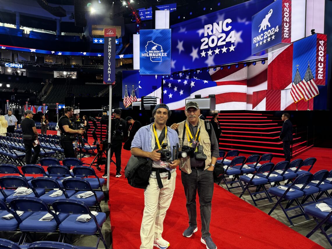 Two photographers stand side by side with cameras and press tags around their necks inside the Republican National Convention in Milwaukee, WI.