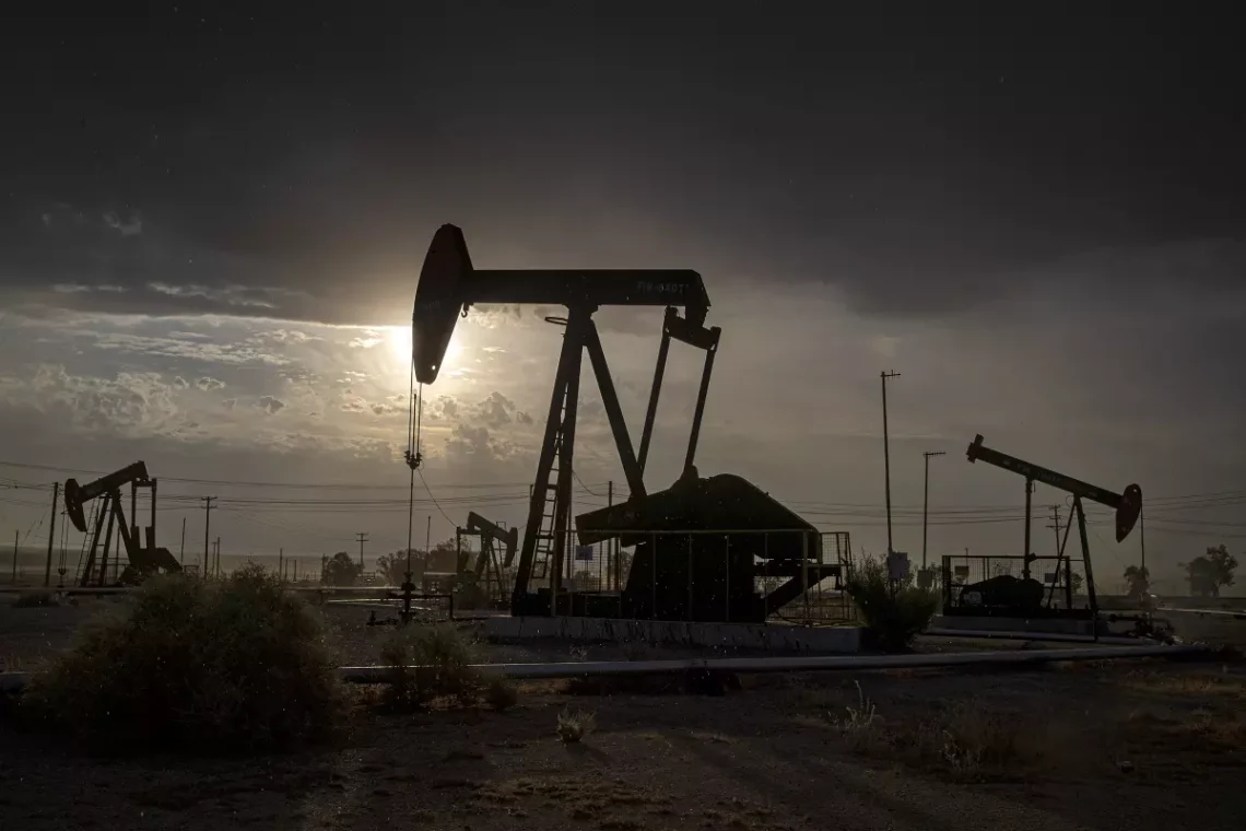 Oil drilling rigs in front of a backdrop of sunrise and telephone wires.