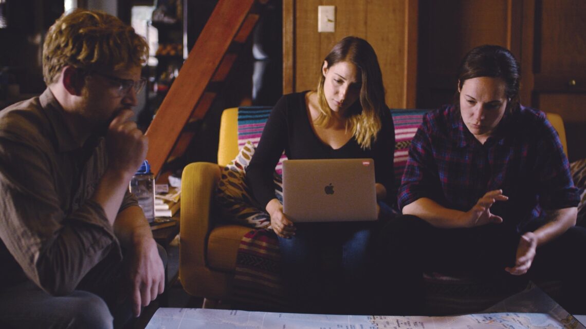 Photo of a man and two women seated together looking focused at their computers.